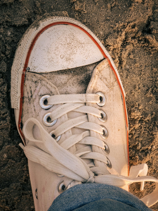 A person wearing white sneakers standing on a dirt ground