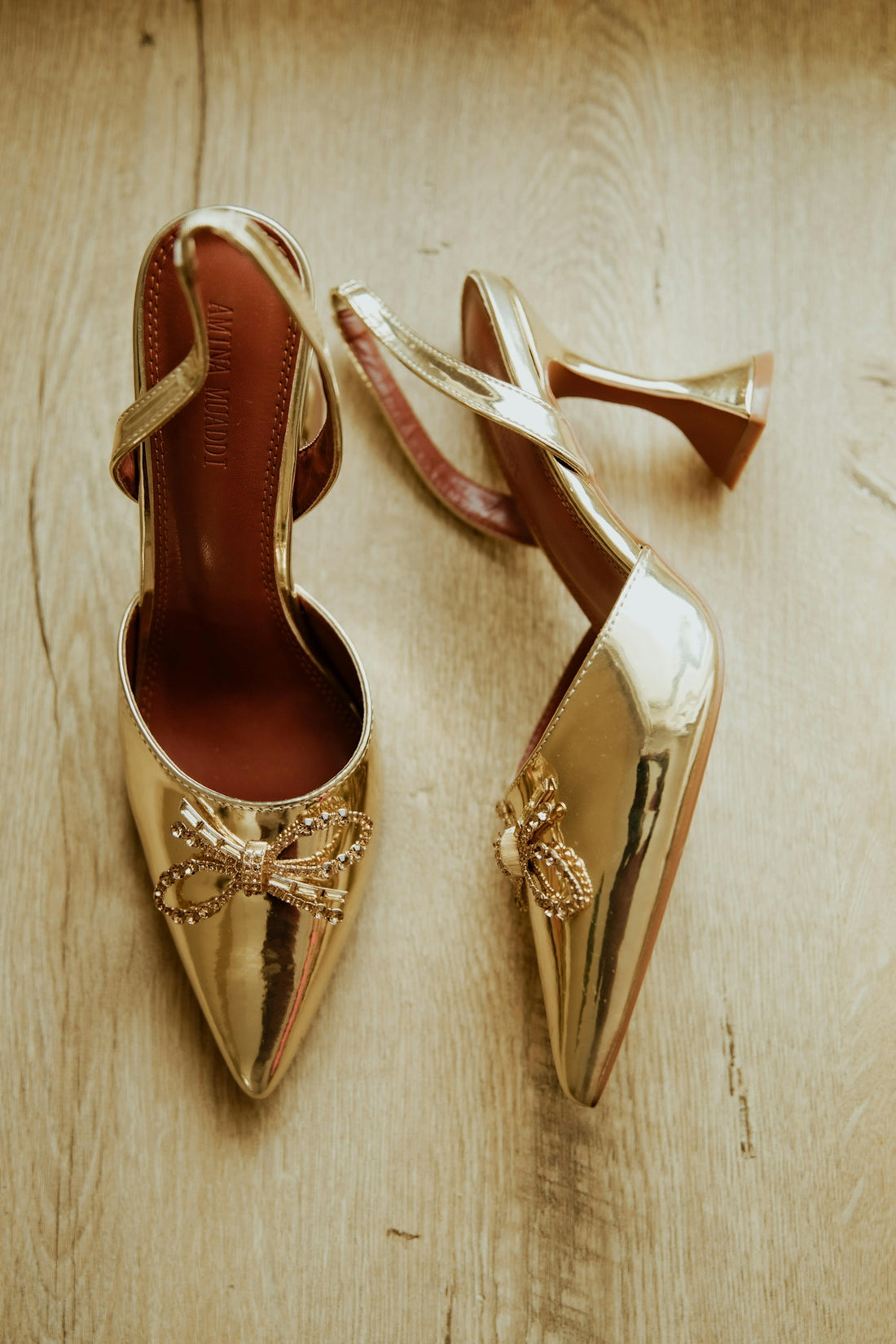 Gold high heels with decorative bows and bees on wood.