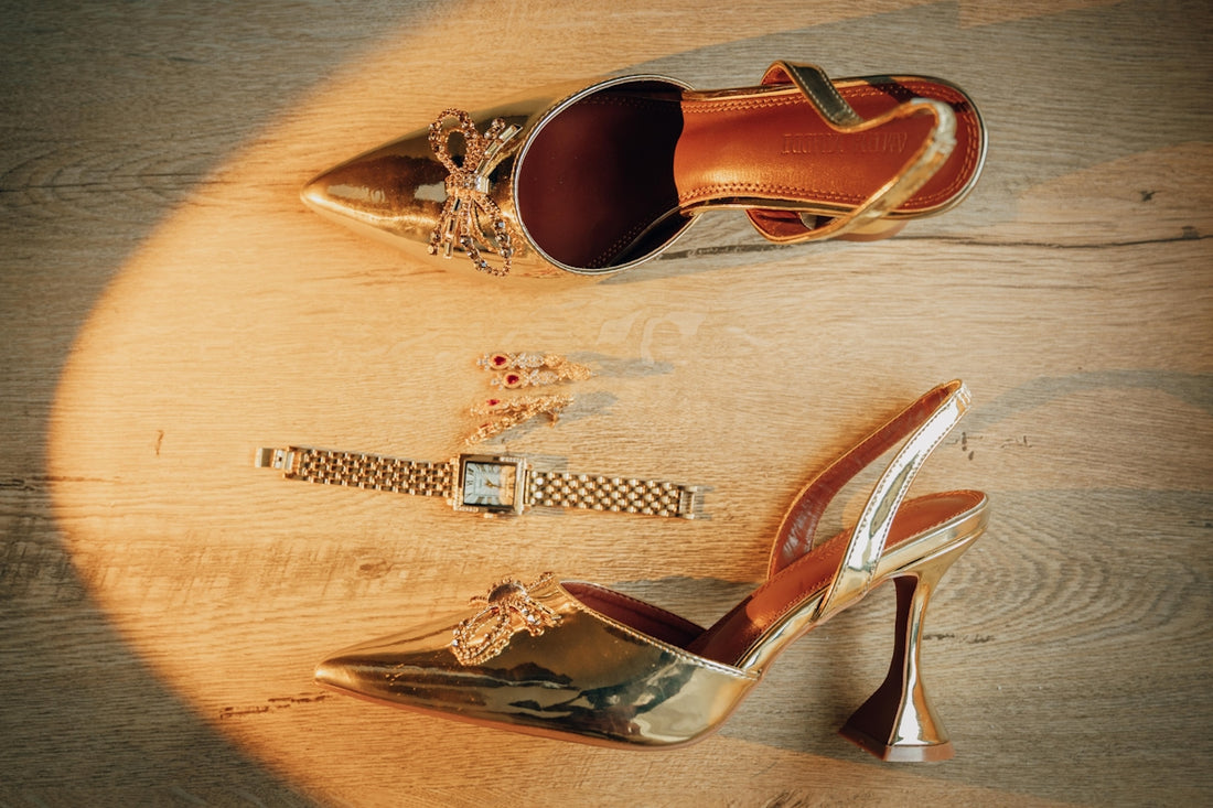 Golden high heels and a watch on a wooden floor.