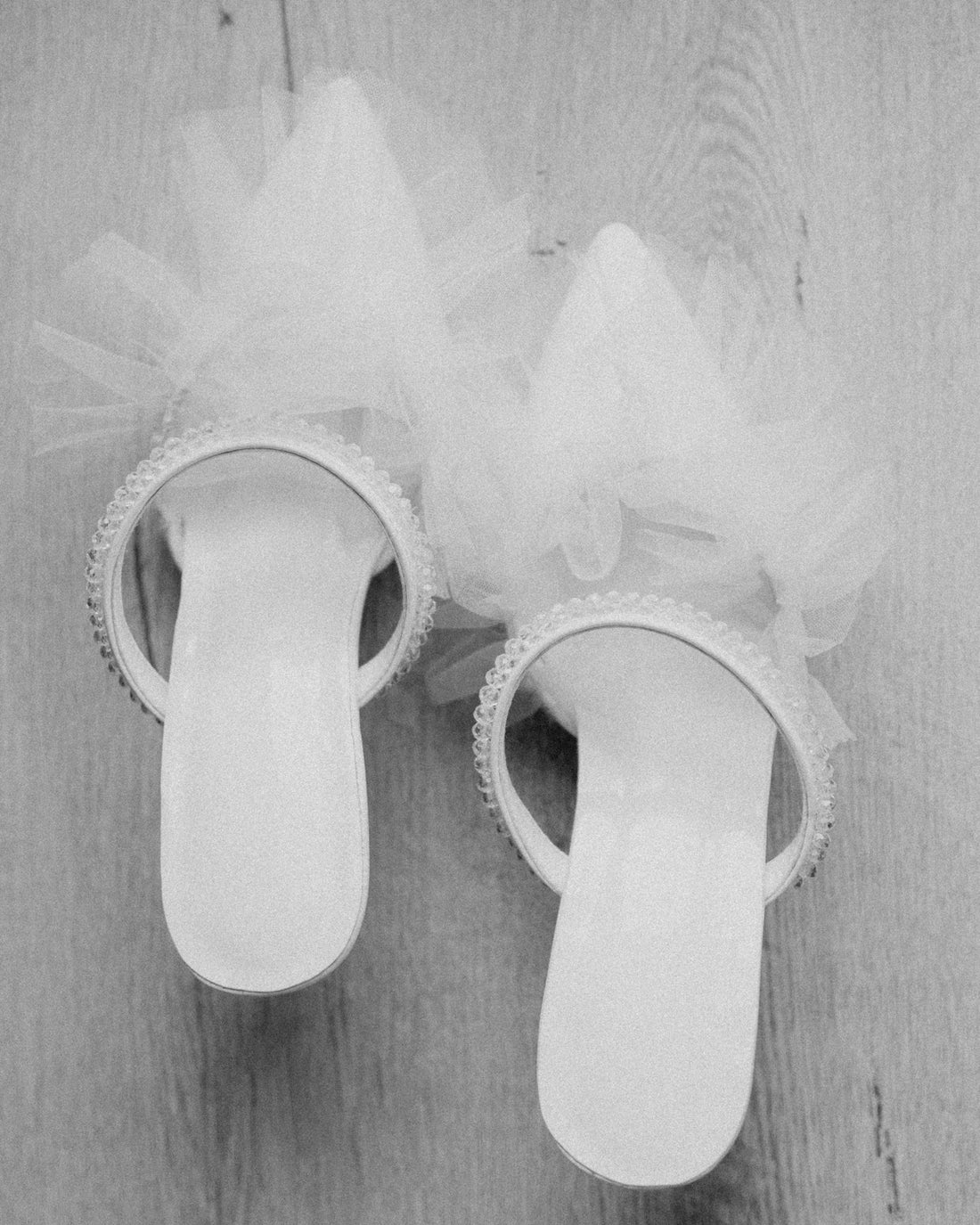 Two white elegant high-heeled shoes with tulle on wood.